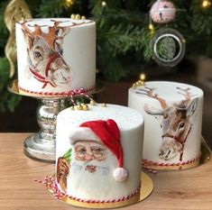 three christmas cakes decorated with santa claus and reindeer images on them, sitting next to a christmas tree