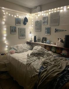 an unmade bed in a room with lights on the wall and pictures above it