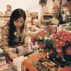 a woman sitting at a table in front of a bunch of books with flowers on it