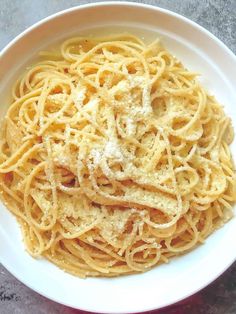 a white bowl filled with pasta on top of a marble countertop and topped with parmesan cheese