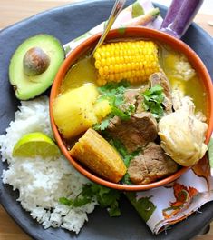 a bowl filled with meat and vegetables next to rice, avocado and corn on the cob