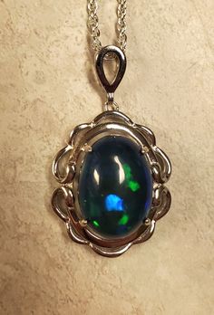 "Beautiful Blue And Green Flash Black Opal, 10.8x14.4mm, 4.8 Carat Ethiopian Smoked Opal, See Video! 925 Sterling Silver Frame Style Pendant, Rhodium Plated, 18\" Sterling Silver Chain. Chain Length Options Available By Messaging Seller At Time Of Purchase. Velvet Necklace Box Included." Oval Blue High Luster Jewelry, High Luster Blue Jewelry For Anniversary, Formal High Luster Blue Jewelry, Formal Blue High Luster Jewelry, High Luster Sterling Silver Jewelry In Silver, Silver Oval Cabochon Necklace For Formal Occasions, High Luster Sterling Silver Jewelry, Oval Sapphire Cabochon Necklace, Oval Sapphire Necklace With Cabochon Cut