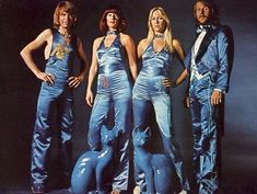 three women in blue outfits standing on stage with their hands on their hipss and one man's head turned to the side