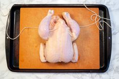 a raw chicken sitting on top of a cutting board next to a knife and string