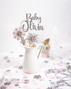 a baby's birth cake topper in a white pitcher on a pink and gray tablecloth