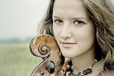 a woman with long hair holding a violin in her right hand and looking at the camera