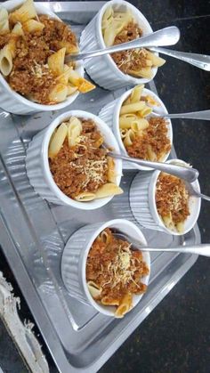 four cups filled with pasta and meat on top of a plastic tray next to utensils