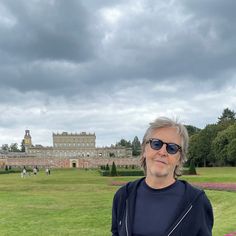 a man standing in front of a large building on top of a lush green field