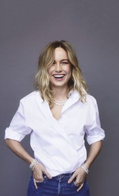 a woman in white shirt and jeans posing with her hands on her hips, smiling at the camera