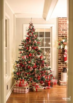 a cat sitting in front of a christmas tree with presents on the floor next to it