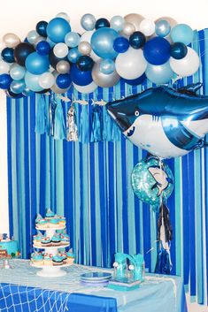 a blue and white birthday party with shark balloons, streamers and desserts on the table