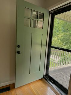 an empty room with a green door and wooden floor next to a large glass window