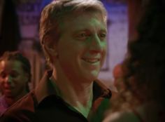 a man smiling while standing in front of other people at a bar with green light on his face