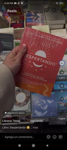 a person holding up a red book in front of bookshelves with spanish words on them