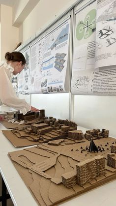 a woman is looking at some model buildings on a table with posters in the background