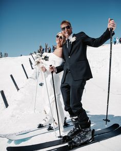 a bride and groom posing for a photo on skis in the snow with people behind them