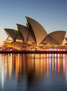 the sydney opera house lit up at night with bright lights reflecting in the water below