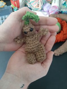 a person holding a tiny teddy bear in their hand with yarn on the table behind them