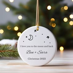 a personalized ornament hanging from a christmas tree with lights in the background