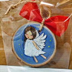 a wooden ornament with an angel painted on it's face and red ribbon