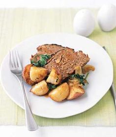 a white plate topped with meat, potatoes and spinach next to an egg on a table