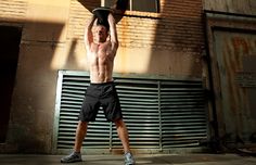 a shirtless man holding a skateboard over his head in front of a building