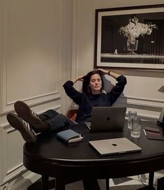 a woman sitting at a table in front of a laptop computer with her hands on her head