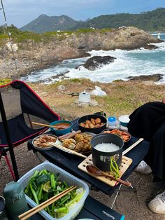 a person sitting at a picnic table with food and drinks on it near the ocean