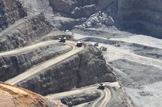 an aerial view of some dirt roads in the middle of a mountain range with trucks driving on it