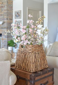 a wicker basket with flowers in it sitting on top of an old trunk next to a couch