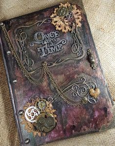 an altered book with gears and chains on the cover is sitting on a piece of fabric