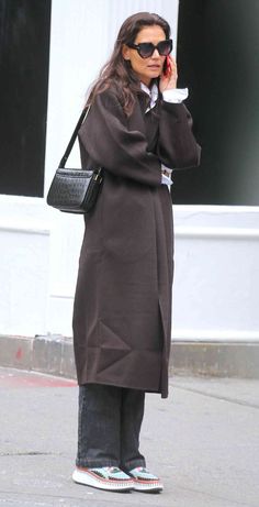 a woman standing on the street talking on her cell phone and holding a purse in one hand