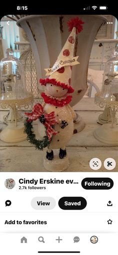 a snowman with a christmas hat and wreath on it's head, standing in front of a vase