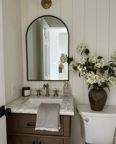 a white toilet sitting next to a sink in a bathroom under a large round mirror