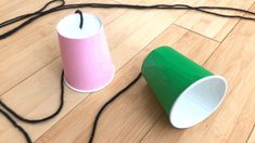 two cups sitting on top of a wooden floor next to a black string and a green one