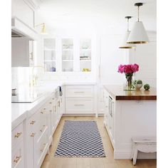 a kitchen with white cabinets and wood flooring next to a rug on the floor