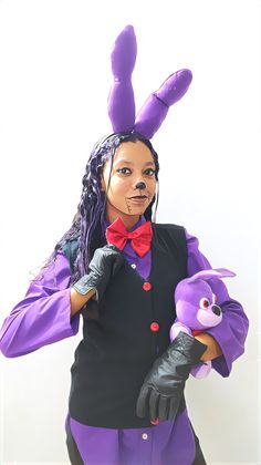 a woman dressed in purple and black is holding a stuffed animal with her hands on her hip