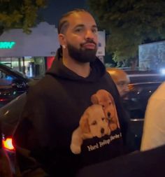 a man with a dog on his hoodie standing in front of a car at night