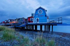 a blue building sitting on top of a wooden pier next to the ocean under a cloudy sky