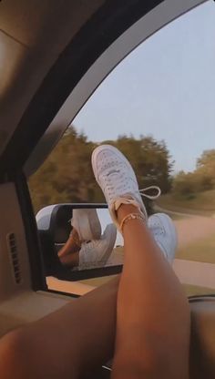 a woman's feet sticking out the window of a car as she drives down a road