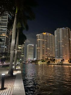 the city is lit up at night along the water's edge with skyscrapers in the background