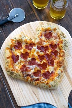 a heart shaped pizza with cheese and pepperoni is on a cutting board next to a glass of beer