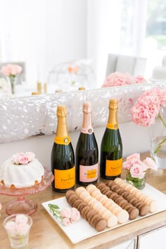 three bottles of champagne are sitting on a table with pastries and flowers in the background