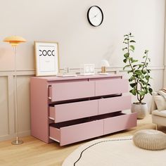 a pink dresser in a living room with a clock on the wall above it and a lamp next to it