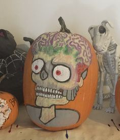 three pumpkins decorated to look like skeletons with faces painted on them, and one has a human skull in the middle