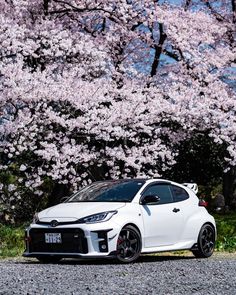 a white car is parked in front of some pink flowers