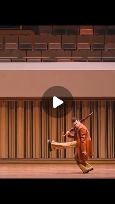 a man in an orange outfit is dancing on the stage with a large wooden chair behind him