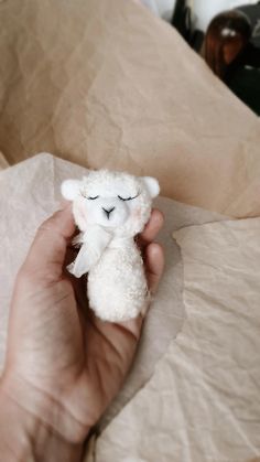 a person holding a small white stuffed animal in their left hand, on top of some brown paper