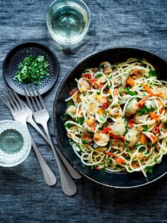 pasta with clams and vegetables in a skillet next to two silver spoons