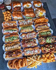 a table topped with lots of trays of food next to french fries and hot dogs